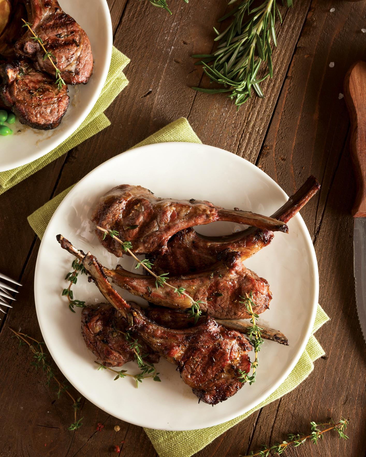 Grilled lamb chops garnished with fresh thyme on a white plate placed on a wooden surface.
